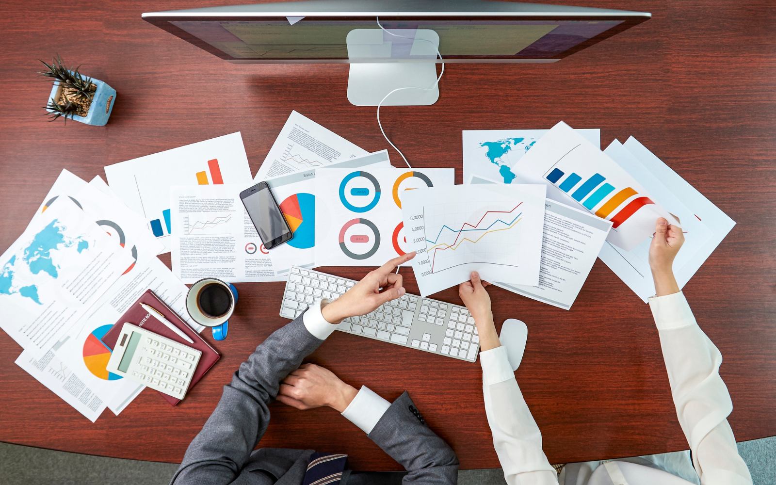 Two colleagues going through printed charts at a desk with a monitor and keyboard
