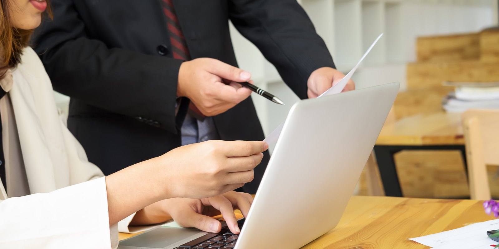 Two colleagues looking at a laptop and a printed report together